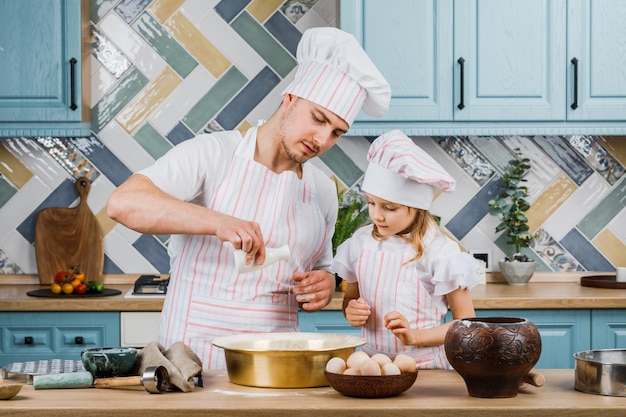 Bambina sveglia e il suo bellissimo papà sorridenti mentre cucinano in cucina a casa. Il concetto di cucina.