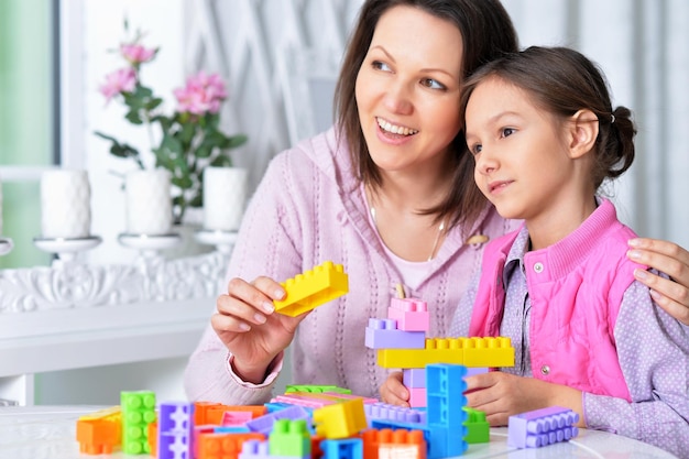 Bambina sveglia e sua madre che giocano blocchi di plastica colorati