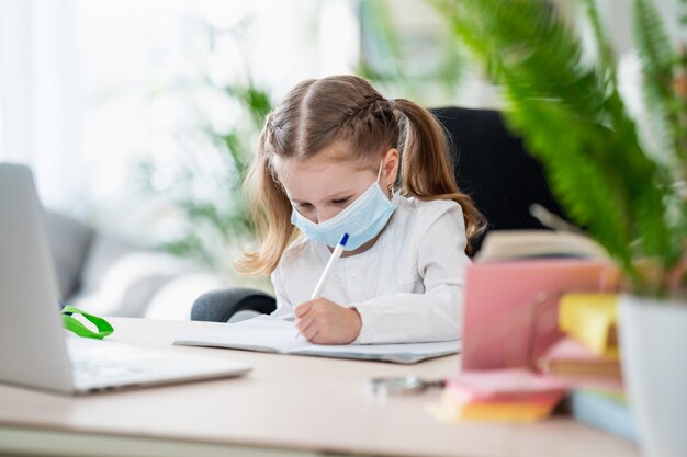 Bambina sveglia, fare i compiti, scrivere nel quaderno, usando il portatile, e-learning