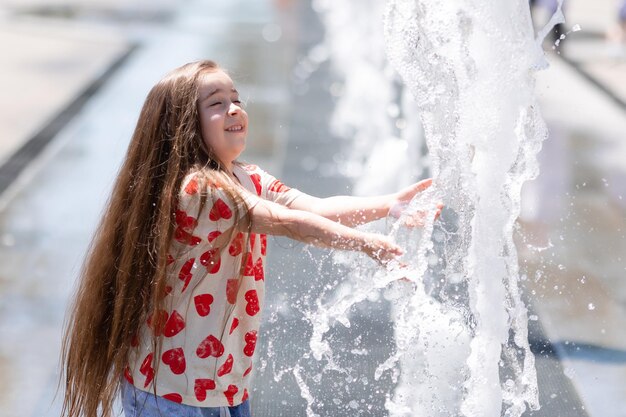 Bambina sveglia in camicia bianca con i cuori che giocano con l'acqua nel parco