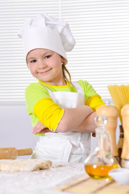 Bambina sveglia in cappello da cuoco che cuoce la torta in cucina