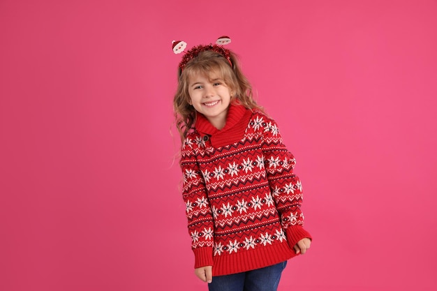 Bambina sveglia in maglione rosso di Natale che sorride su sfondo rosa