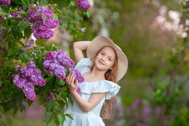 Bambina sveglia in un cappello di paglia in primavera nel giardino lilla