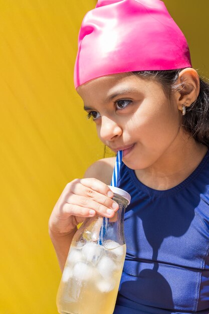 Bambina sveglia in un costume da bagno che prende il sole mentre beve una limonata