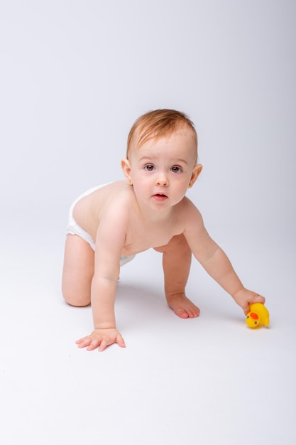 Bambina sveglia in un pannolino che gioca con un'anatra giocattolo di gomma isolata su sfondo bianco