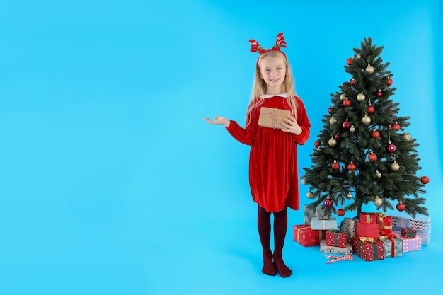 Bambina sveglia su sfondo blu con albero di Natale e regali