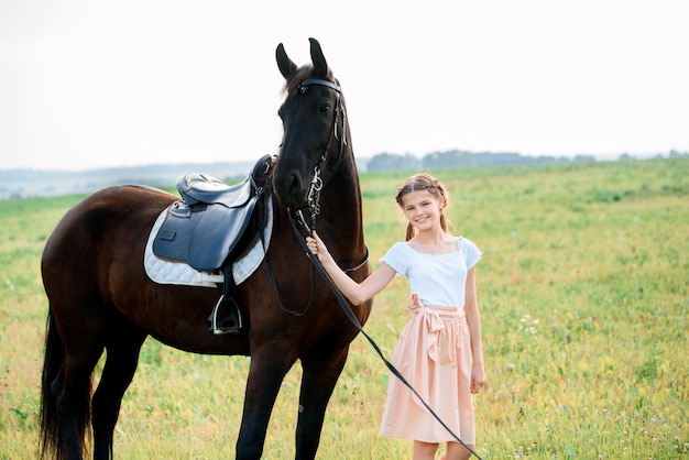 Bambina sveglia su un cavallo in un vestito da campo estivo