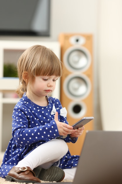 Bambina sveglia sul cellulare di uso del tappeto del pavimento