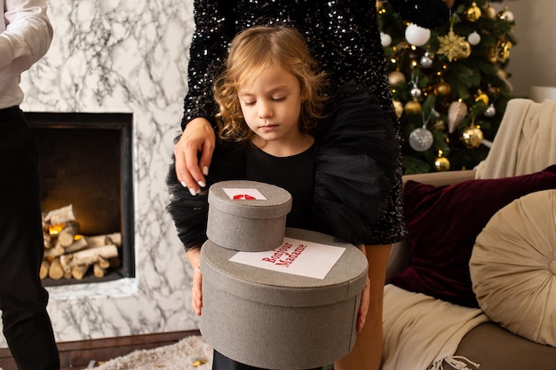 Bambina sveglia sullo sfondo di alberi di Natale e luci con scatole regalo nelle sue mani