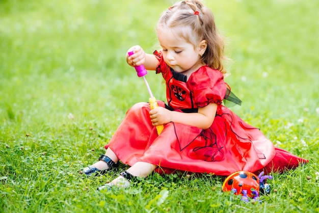Bambina sveglia vestita con un lungo vestito rosso che gioca e si diverte su un prato verde