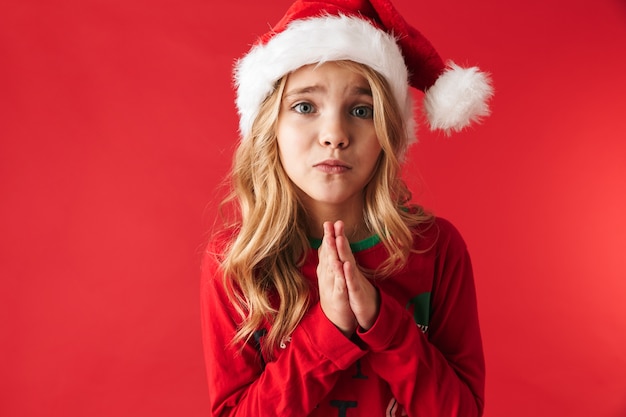 Bambina triste che indossa il cappello di Natale in piedi isolato, chiedendo un regalo
