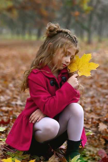 Bambina triste che si siede sulla terra in foglie cadute.