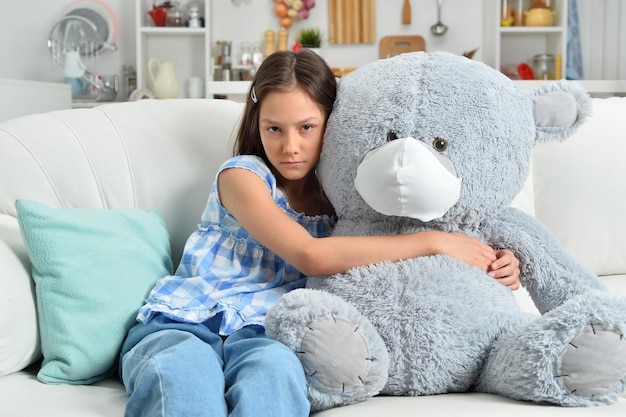 Bambina triste con orso giocattolo in maschera facciale