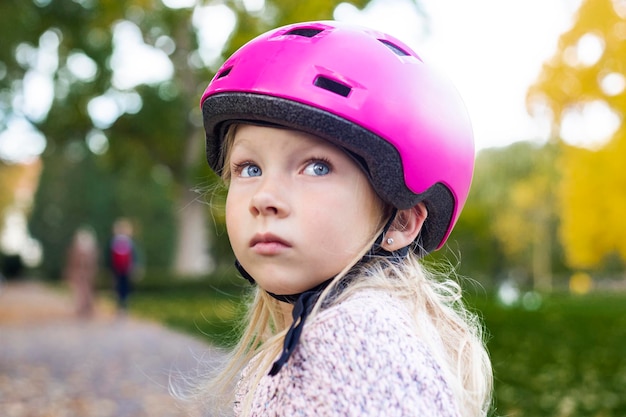 Bambina triste in un casco rosa nel parco