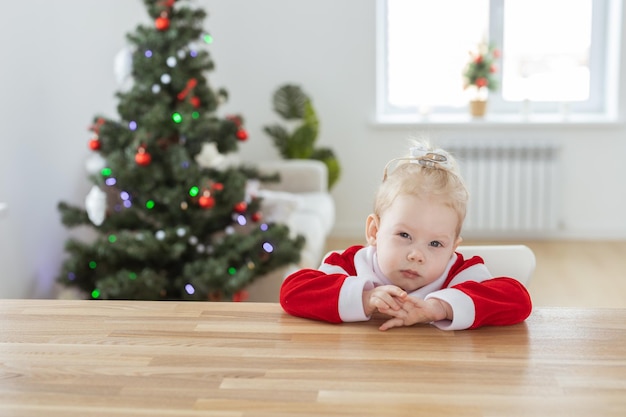 Bambina vestita in abito natalizio con impianti cocleari divertendosi a casa con sfondo albero di Natale e copia spazio apparecchio acustico e tecnologie innovative per il trattamento della sordità