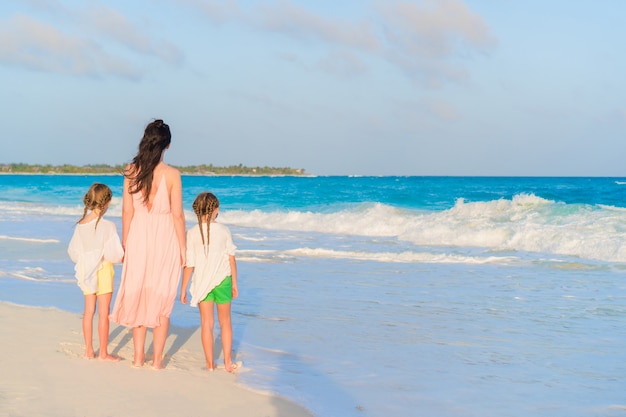 Bambine adorabili e giovane madre sulla spiaggia bianca sul tramonto