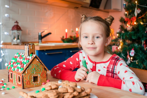 Bambine che producono la casa di pan di zenzero di Natale al camino in salone decorato.