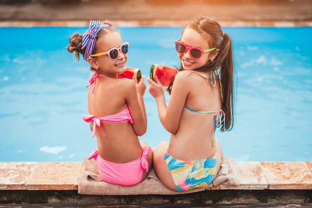 Bambine contente con fette di anguria a bordo piscina nella soleggiata giornata estiva