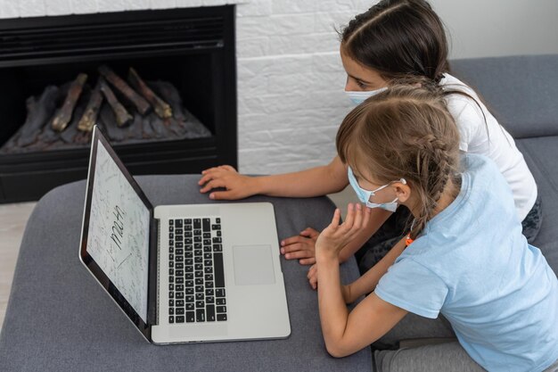 Bambine della scuola che studiano a casa indossando maschera, apprendimento a distanza.