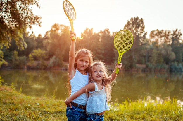 Bambine divertirsi all'aperto dopo aver giocato a badminton. Le sorelle alzano racchette nel parco di primavera.