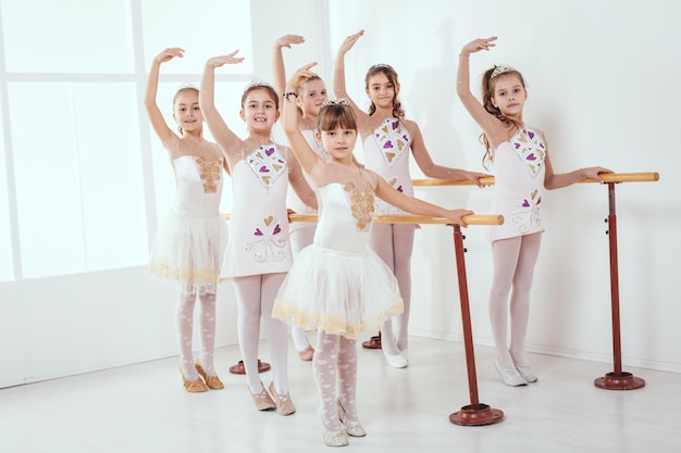 Bambine sorridenti che usano la sbarra mentre praticano nello studio di danza. Guardando la fotocamera.