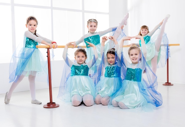 Bambine sorridenti in abiti che praticano posture durante la lezione di danza classica. Guardando la fotocamera.