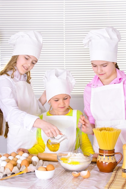 Bambine sveglie in cappelli e grembiuli da chef che preparano la pasta in cucina
