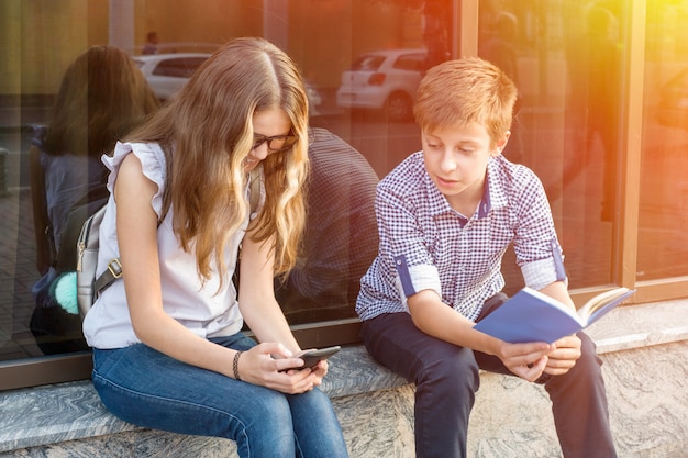 Bambini adolescenti, libro di lettura e utilizzo dello smartphone.