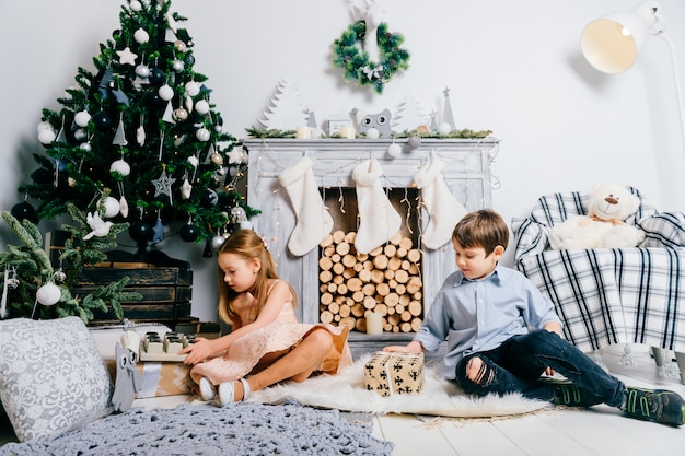 Bambini adorabili che giocano nella stanza con l'albero e il camino di cristmas. Concetto di vacanze invernali.