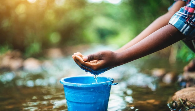 Bambini africani desolati con le mani nude e usurate che afferrano un secchio d'acqua vicino a un ruscello che simboleggia il pove