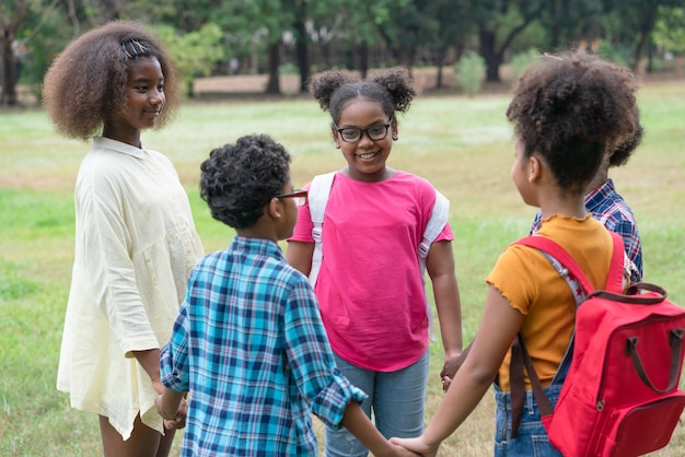 Bambini afroamericani che stanno insieme e che si tengono per mano nel cerchio nel parco, concetto all'aperto di istruzione