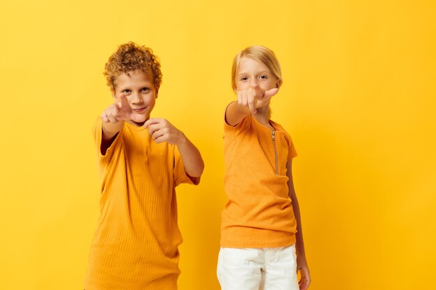 Bambini alla moda svegli in magliette gialle che stanno fianco a fianco le emozioni dell'infanzia hanno isolato lo sfondo inalterato