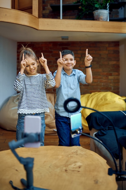 Bambini allegri blogger ballano sulla macchina fotografica, piccoli vlogger. Blogging per bambini in home studio, social media per un pubblico giovane, trasmissione Internet online