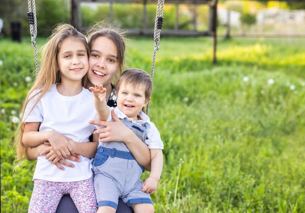 Bambini allegri in abiti leggeri cavalcano un'altalena in un giardino fiorito e ridono con un sorriso felice