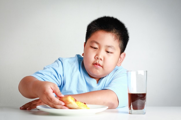 Bambini asiatici grassi stanno mangiando la pizza su un tavolo bianco con nettare di soda. Sfondo bianco. Concetti di controllo del peso del bambino