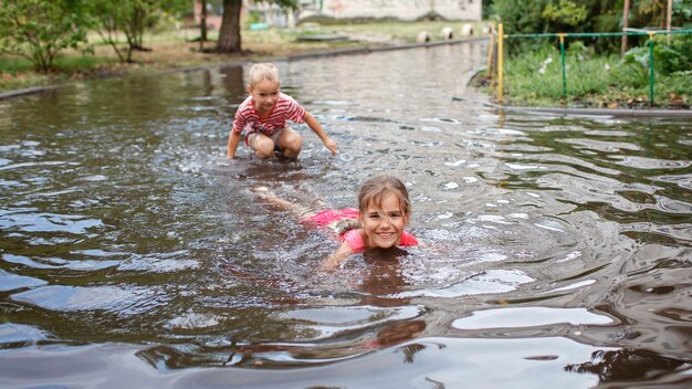 Bambini carini che saltano e nuotano nelle pozzanghere dopo la calda pioggia estiva felice infanzia