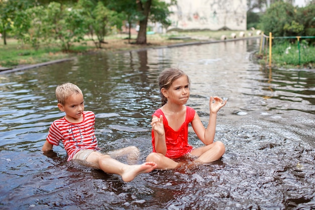 Bambini carini che saltano e nuotano nelle pozzanghere dopo la calda pioggia estiva felice infanzia