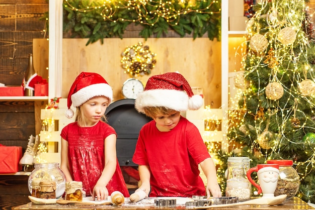 Bambini carini in cappelli di Babbo Natale che preparano golosità natalizie