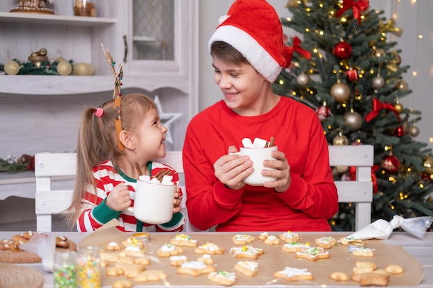 bambini carini in pigiama natalizio rosso con in mano una tazza di cacao con marshmallow seduti sulla cucina