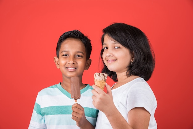 Bambini carini indiani o asiatici che mangiano gelato o barretta di mango o caramelle. Isolato su sfondo colorato