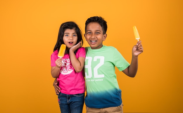 Bambini carini indiani o asiatici che mangiano gelato o barretta di mango o caramelle. Isolato su sfondo colorato