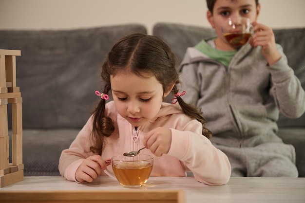 Bambini caucasici - ragazzo e ragazza, che bevono tisane mentre riposano dopo aver costruito strutture in legno da mattoni e blocchi di legno a casa. Sviluppo delle capacità motorie fini, concetto di giochi da tavolo educativi