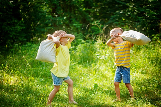 Bambini che combattono insieme ai cuscini in un giardino estivo soleggiato