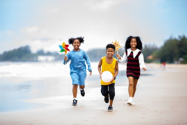 Bambini che giocano a correre sulla sabbia in spiaggia, un gruppo di bambini che si tengono per mano in fila sulla spiaggia in estate, vista posteriore contro il mare e il cielo blu