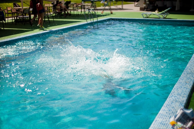 Bambini che giocano in piscina. Spruzzi d'acqua. Bambini che saltano in piscina in una soleggiata giornata estiva