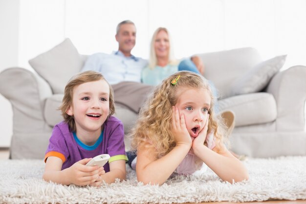 Bambini che guardano la TV mentre i genitori si siedono sul divano