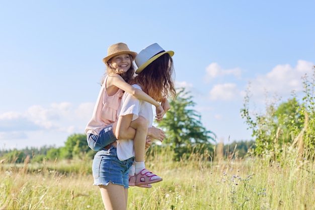 Bambini che ridono felici che giocano nel prato, due sorelle che si divertono nella natura