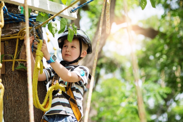 Bambini che scalano nel parco avventura. Il ragazzo ama arrampicarsi nell'avventura del corso di corde. Parco di arrampicata bambino ad alto filo