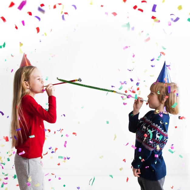 Bambini che suonano trombe da festa con coriandoli che celebrano il nuovo anno