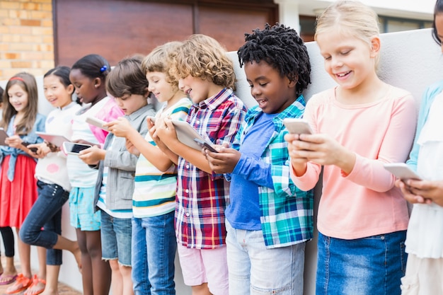 Bambini che utilizzano il telefono cellulare e la tavoletta digitale sul terrazzo della scuola